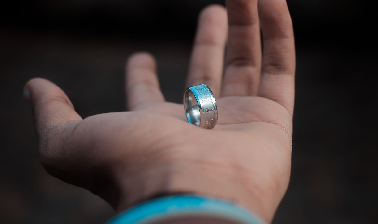 Una mano abierta sosteniendo un anillo de acero con la palabra Jesús grabada