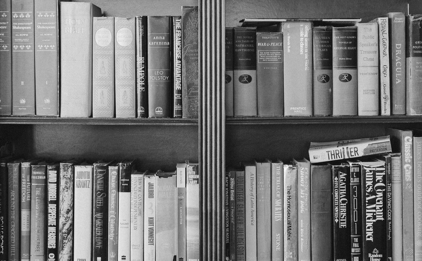 Una estantería antigua llena de libros de lomo oscuro, con la luz entrando de lado