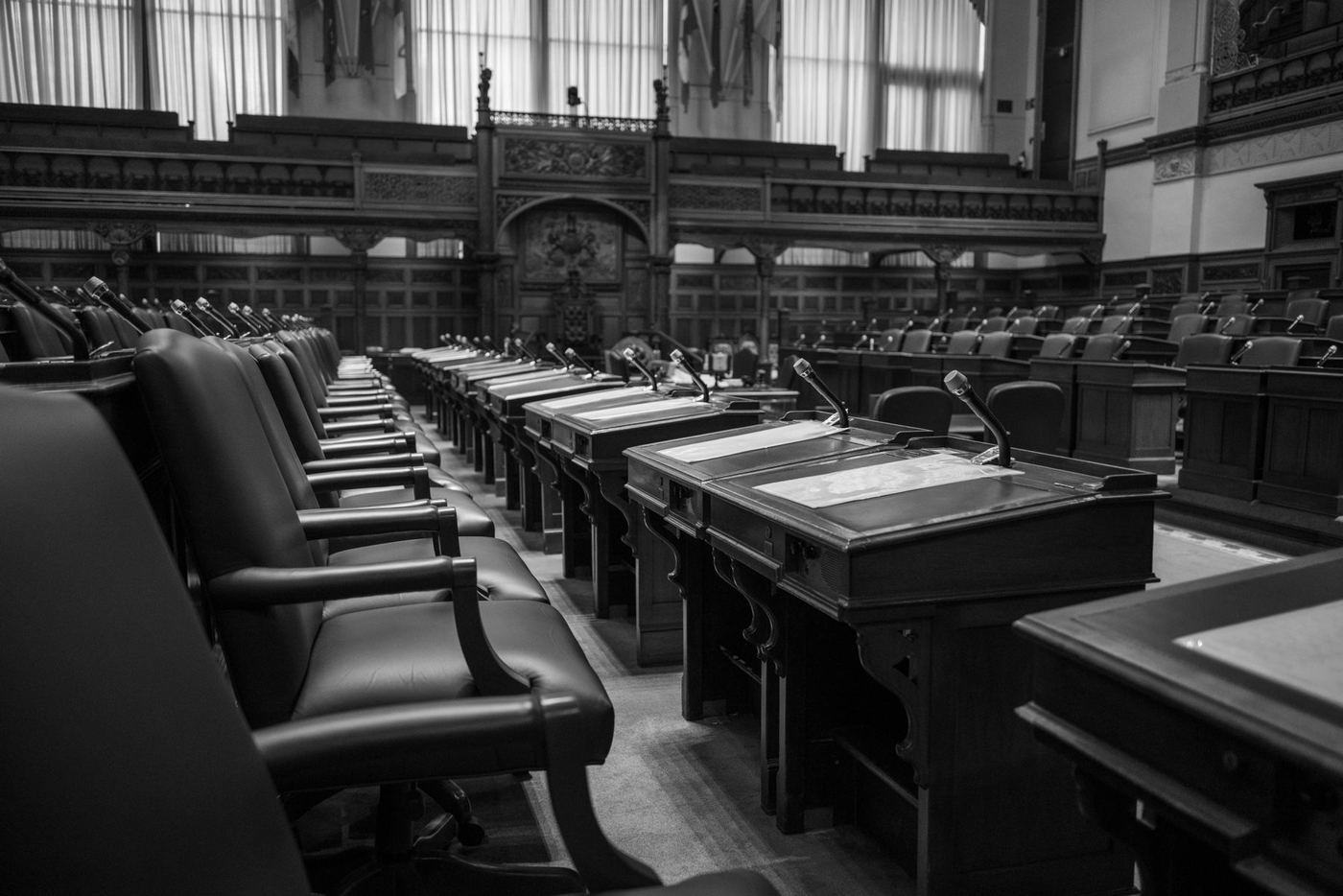 Un recinto legislativo vacío, en blanco y negro, con filas de curules y micrófonos