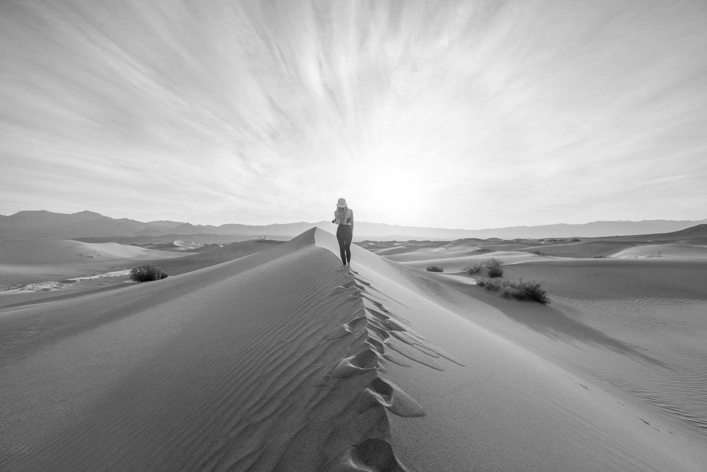 Una figura pequeña camina sola sobre una duna del desierto al amanecer