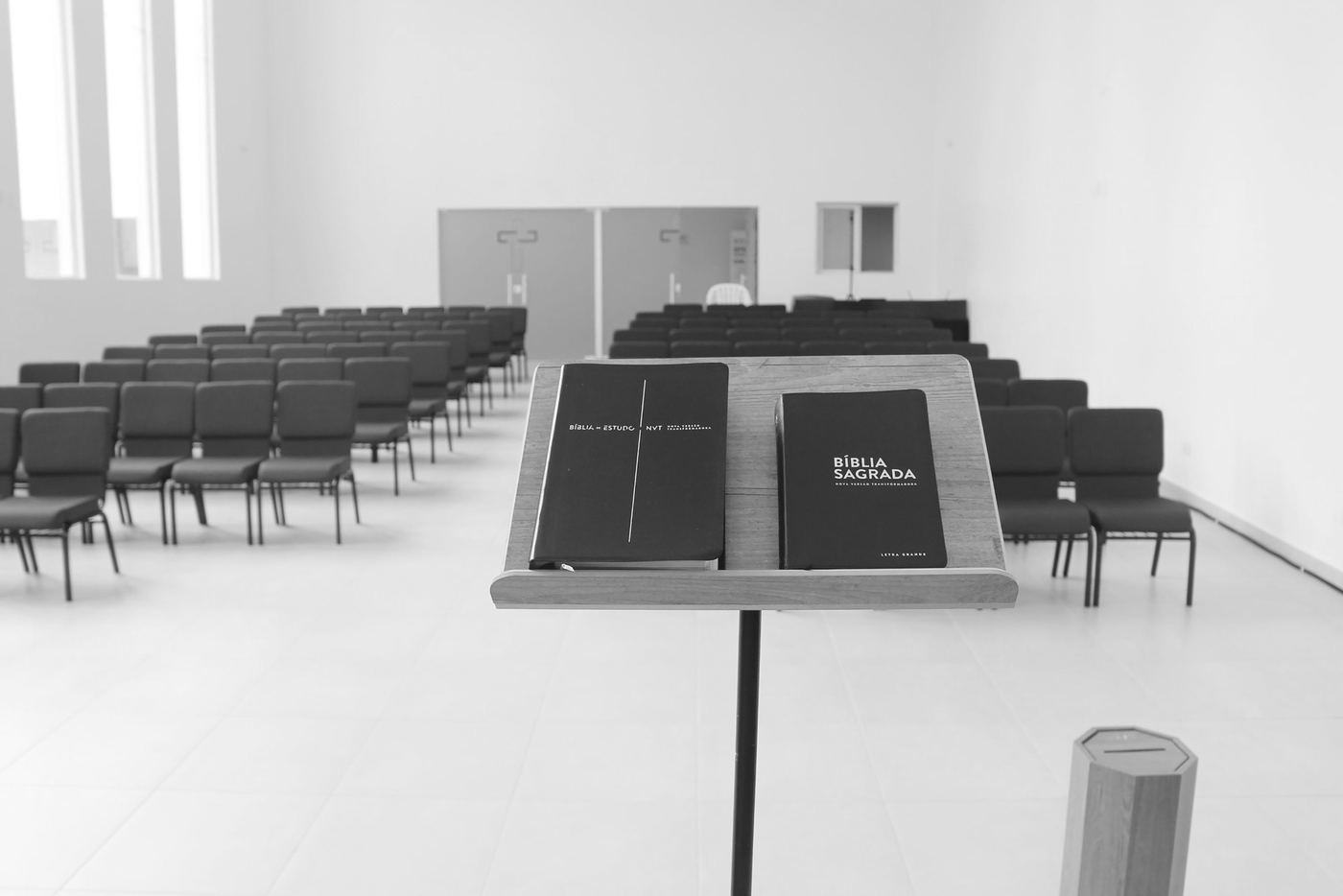 Un salón de iglesia vacío, con sillas rojas en filas y un atril con dos Biblias en primer plano