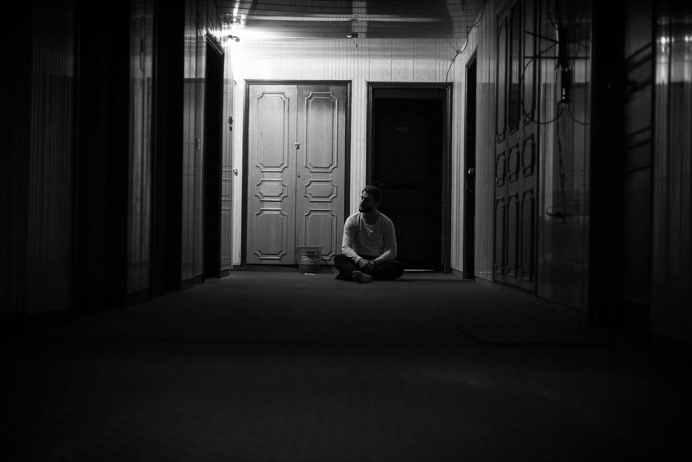 Una persona sentada sola en el suelo, al fondo de un corredor a oscuras