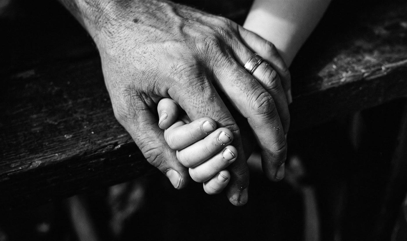 Una mano grande sostiene con firmeza una mano más pequeña, sobre un fondo oscuro
