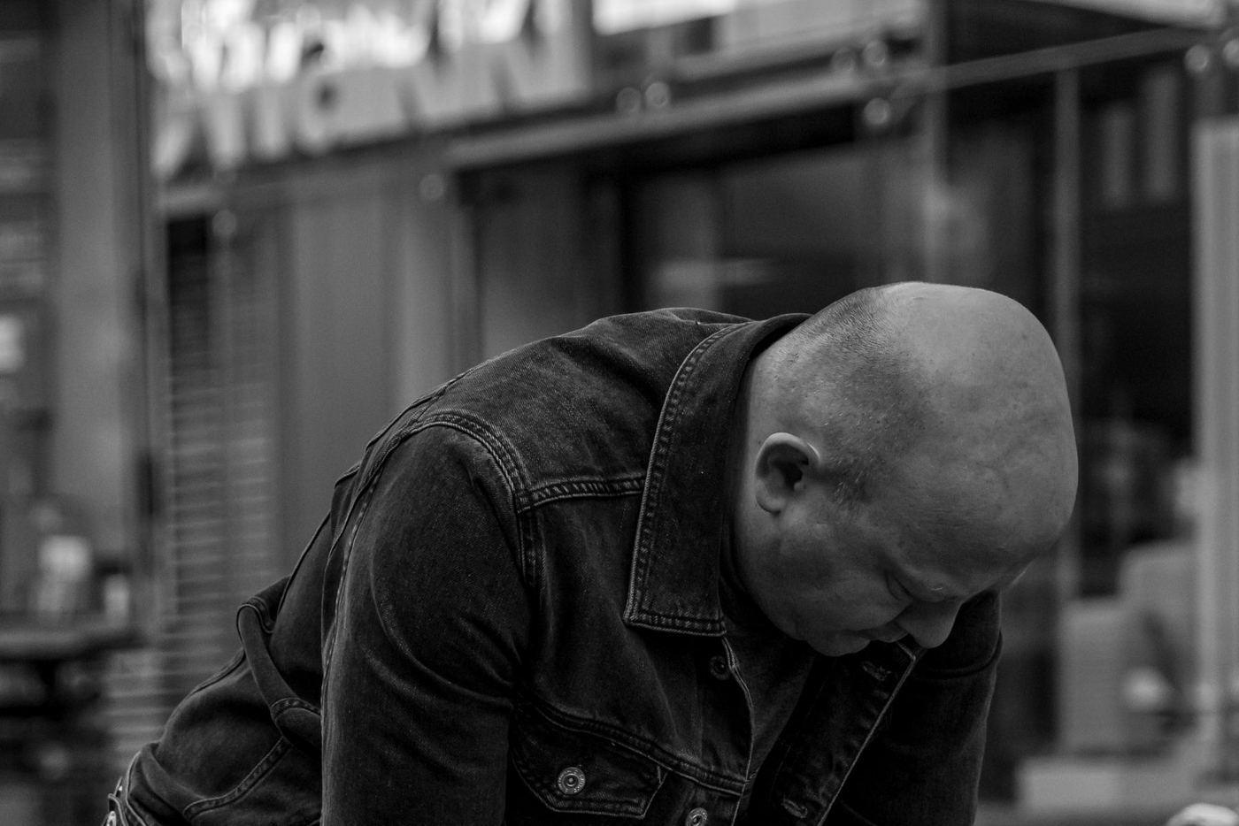 Un hombre encorvado en una banca con la cabeza agachada, en blanco y negro