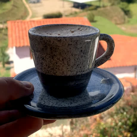 Una taza de café sostenida en la mano, con tejados y montaña al fondo
